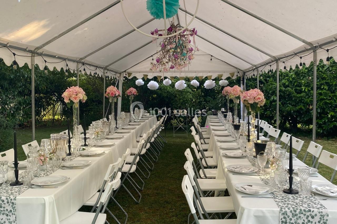 Tente blanche aménagée pour un repas festif avec longues tables dressées, décorations florales et vaisselle élégante.