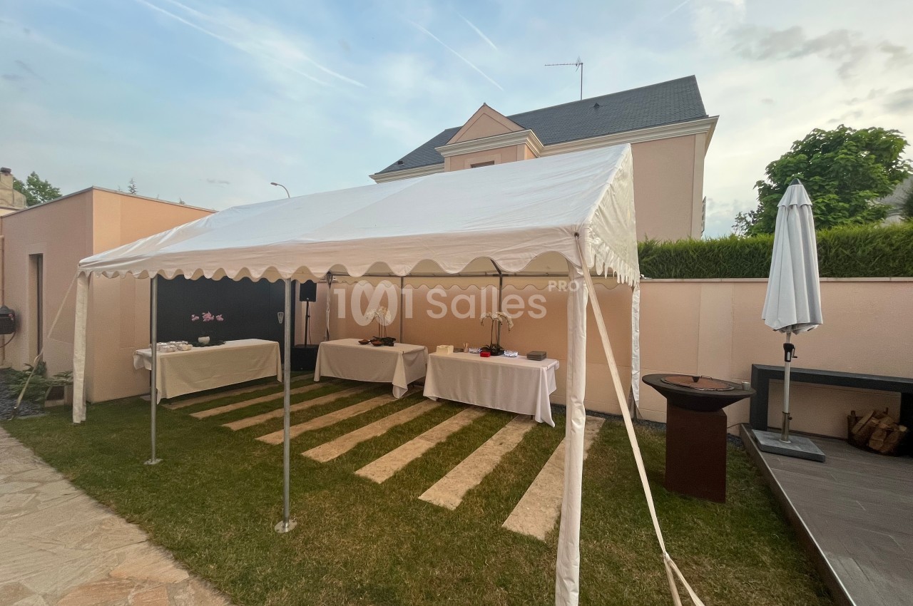 Tente blanche installée dans un jardin avec des tables dressées pour un événement en extérieur.