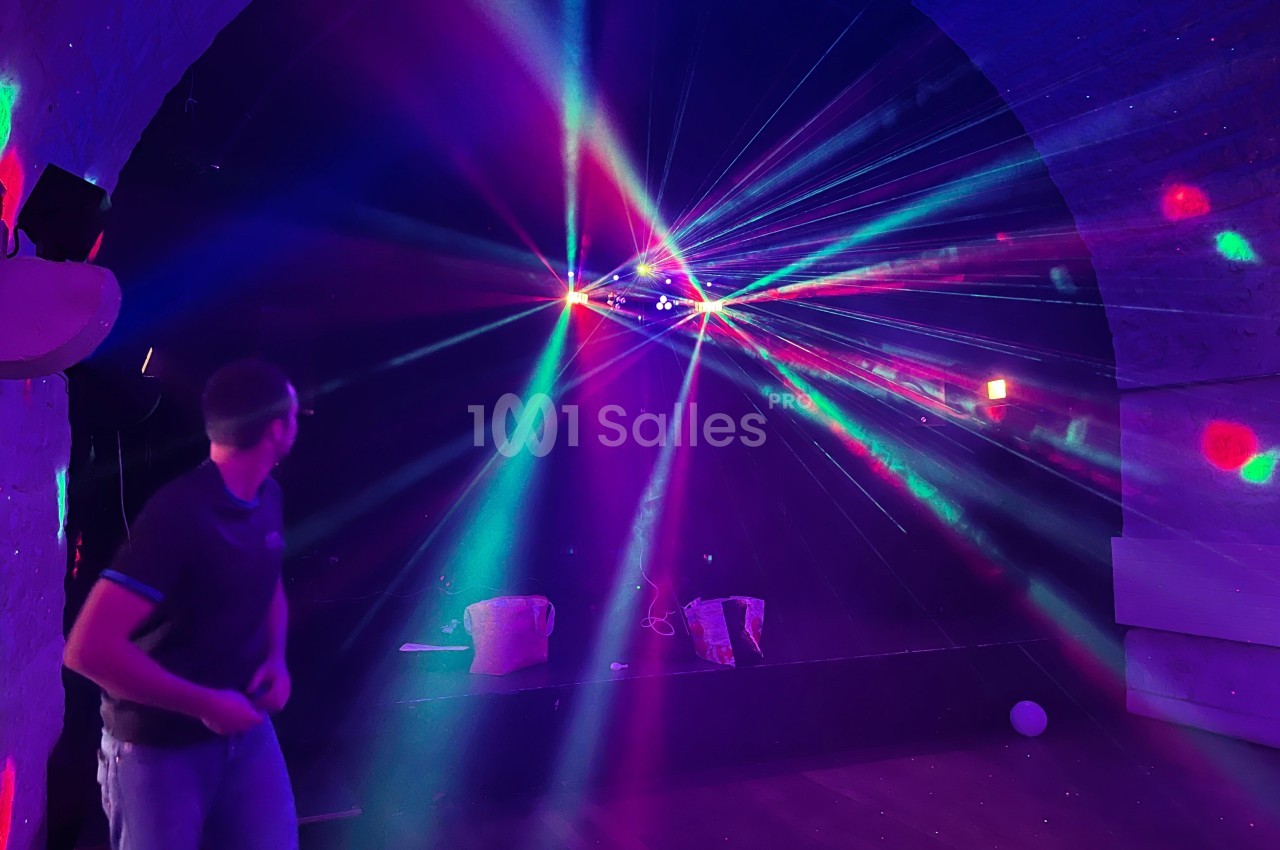 Un homme dans une salle sombre regarde des faisceaux lumineux colorés projetés depuis un système d'éclairage.