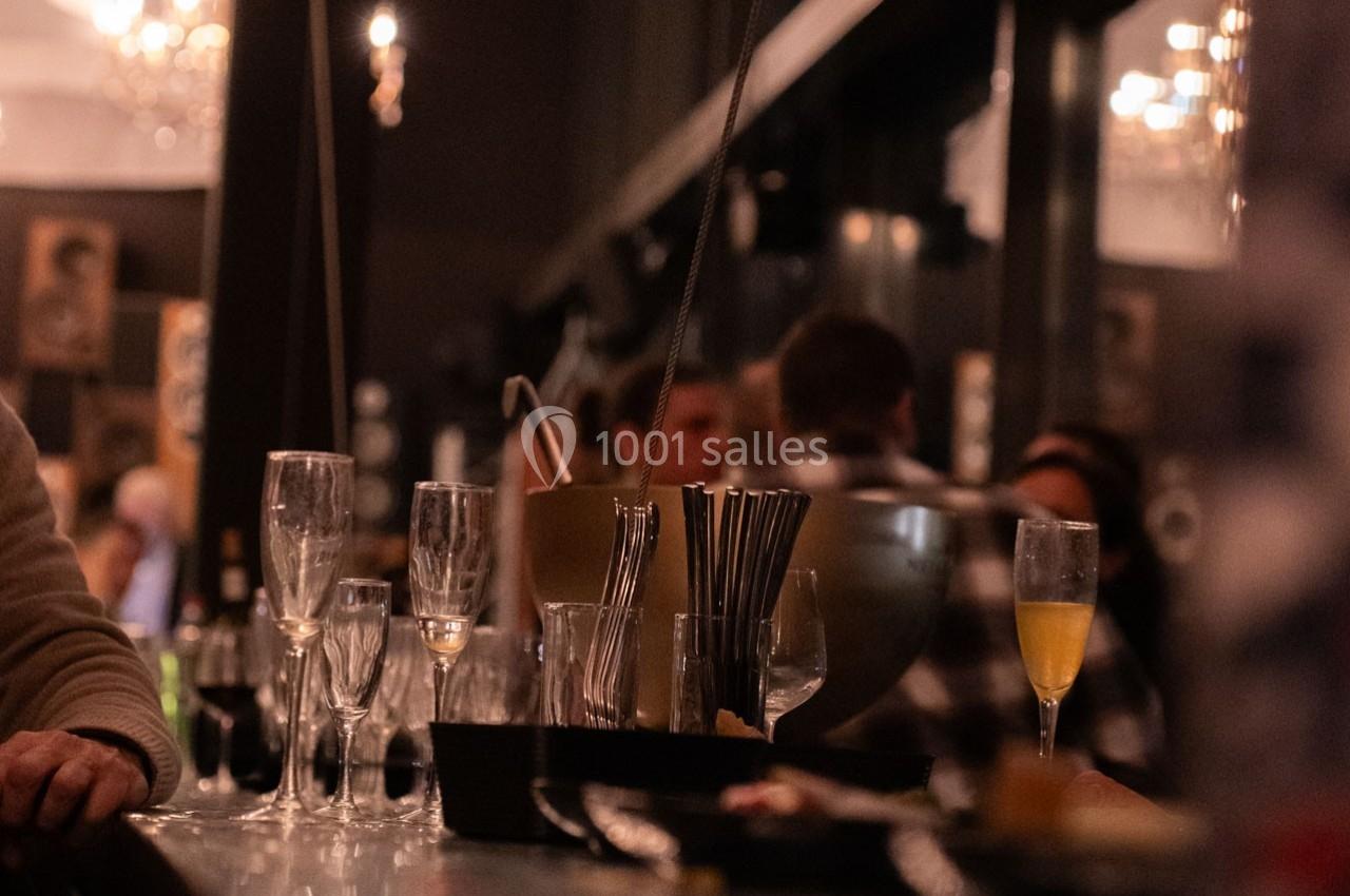 Verres vides et flûtes à champagne sur un comptoir de bar, avec des clients flous en arrière-plan.