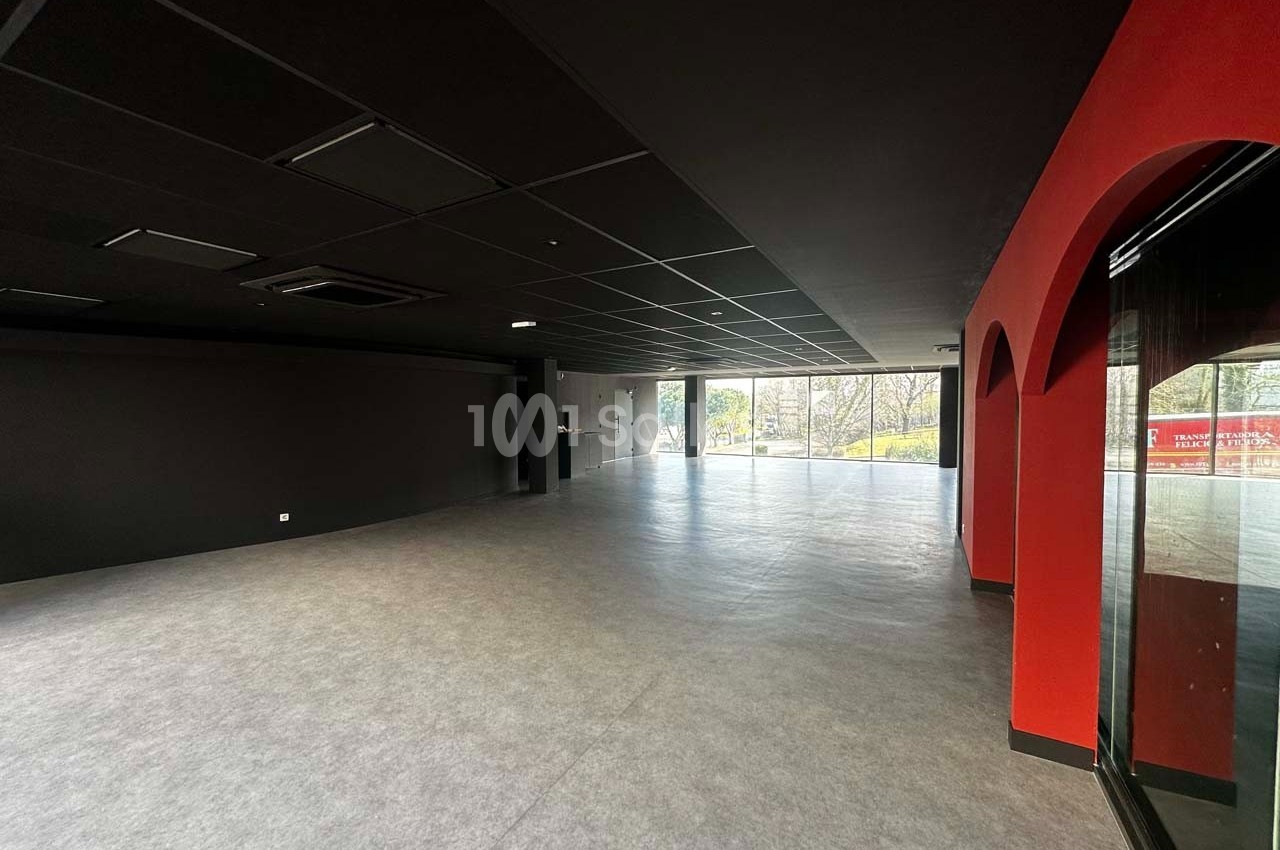 Salle vide avec sol gris, murs noirs et rouges, grandes baies vitrées laissant entrer la lumière naturelle.