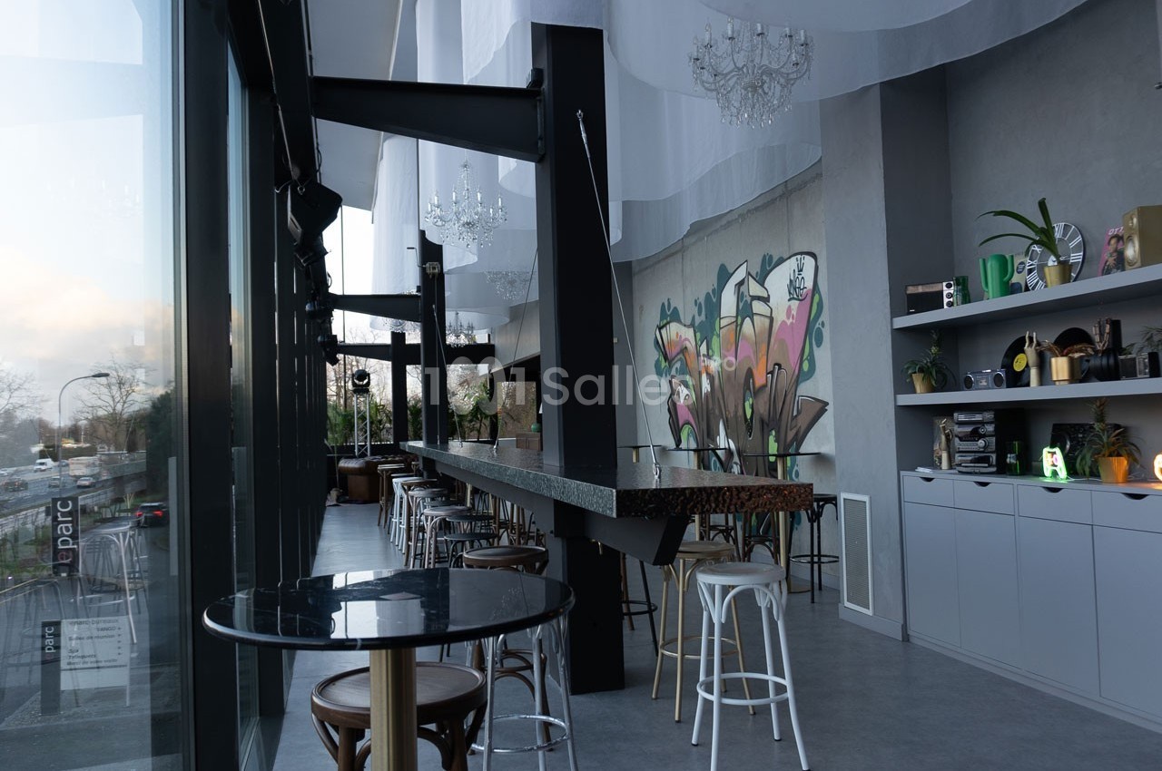 Intérieur d'un café moderne avec un long comptoir, des tabourets, des étagères décorées et une fresque murale colorée.