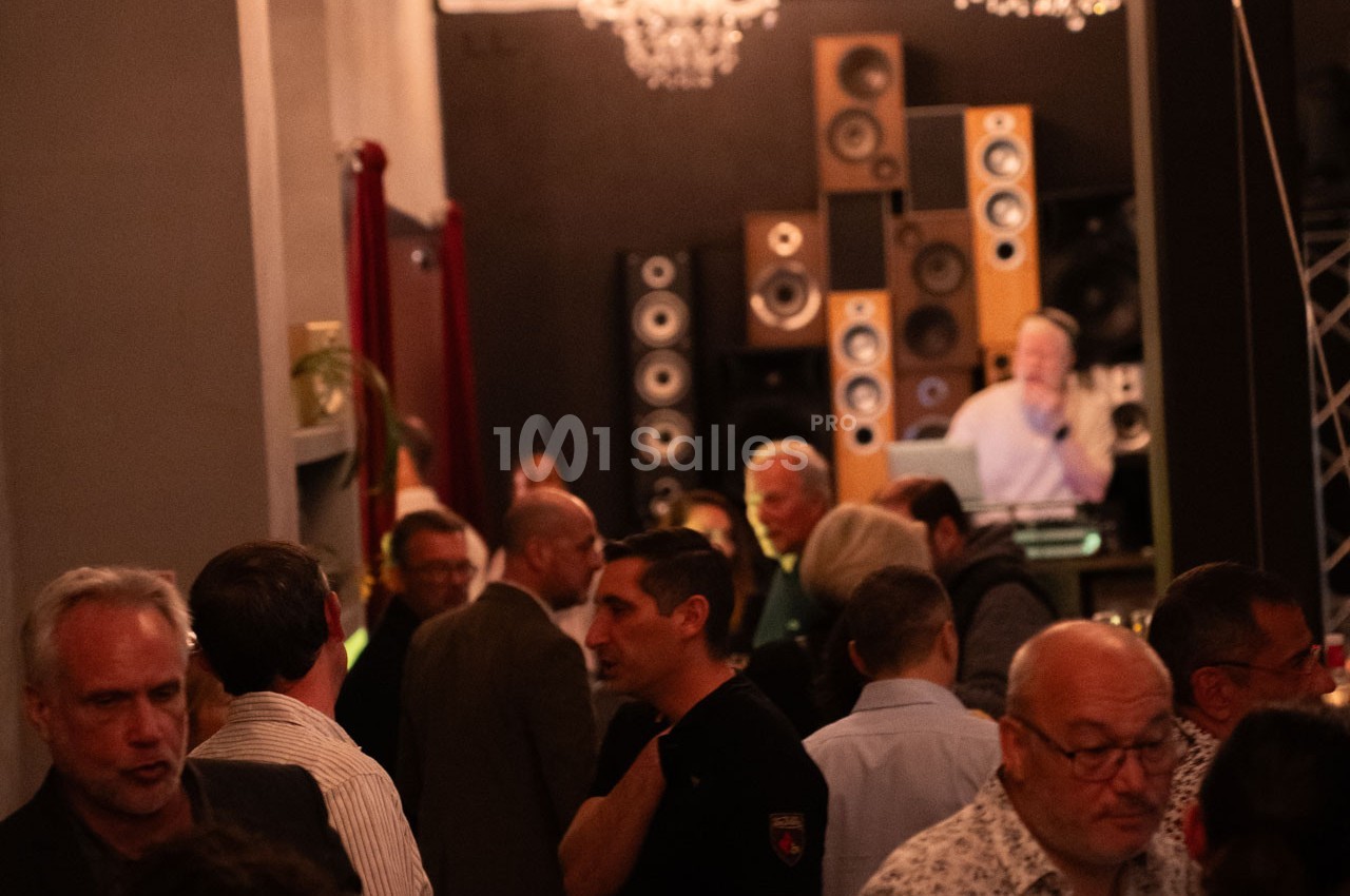 Groupe de personnes discutant dans une salle avec des enceintes empilées en arrière-plan et un DJ à une table de mixage.