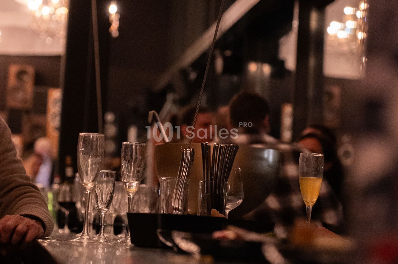 Verres vides et flûtes à champagne sur un comptoir de bar, avec des clients flous en arrière-plan.