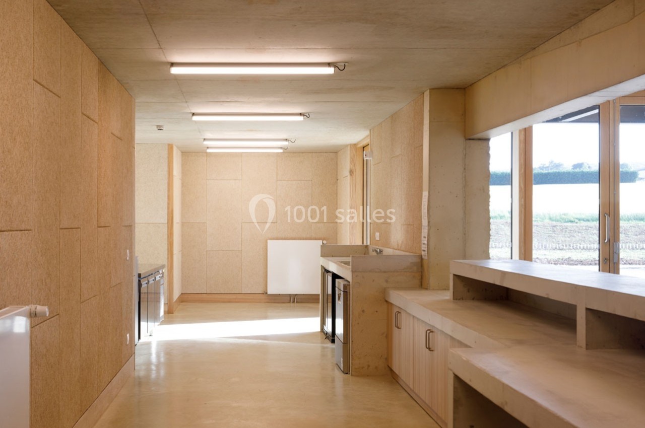 Intérieur d'une pièce lumineuse avec murs en panneaux de bois, plan de travail, fenêtres et vue sur l'extérieur.