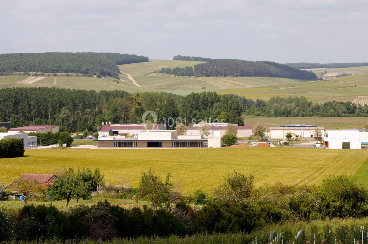 Paysage rural avec des champs cultivés, des bâtiments agricoles et une forêt en arrière-plan sous un ciel partiellement…