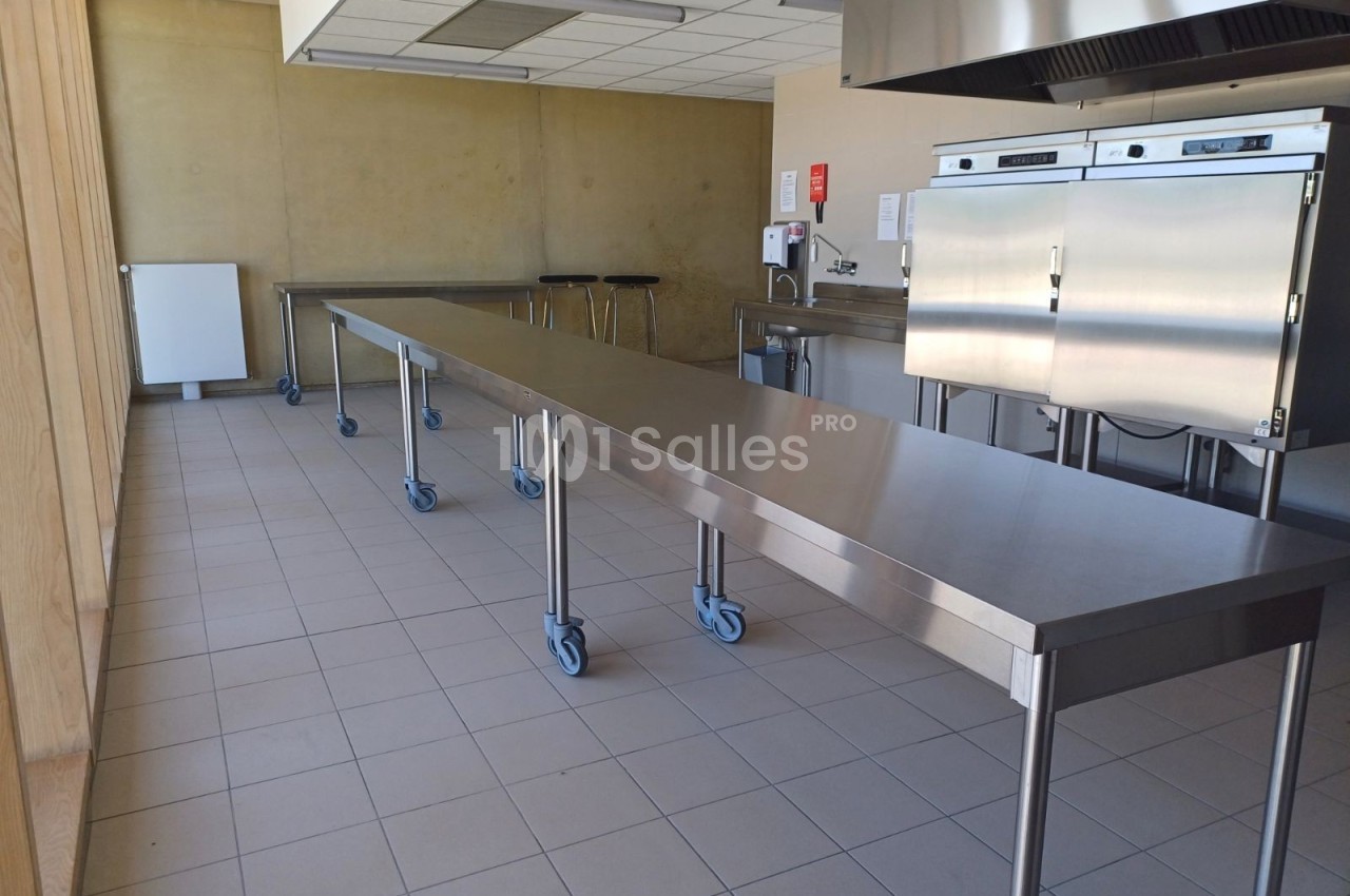Cuisine professionnelle avec plans de travail en inox sur roulettes, four industriel et carrelage au sol.