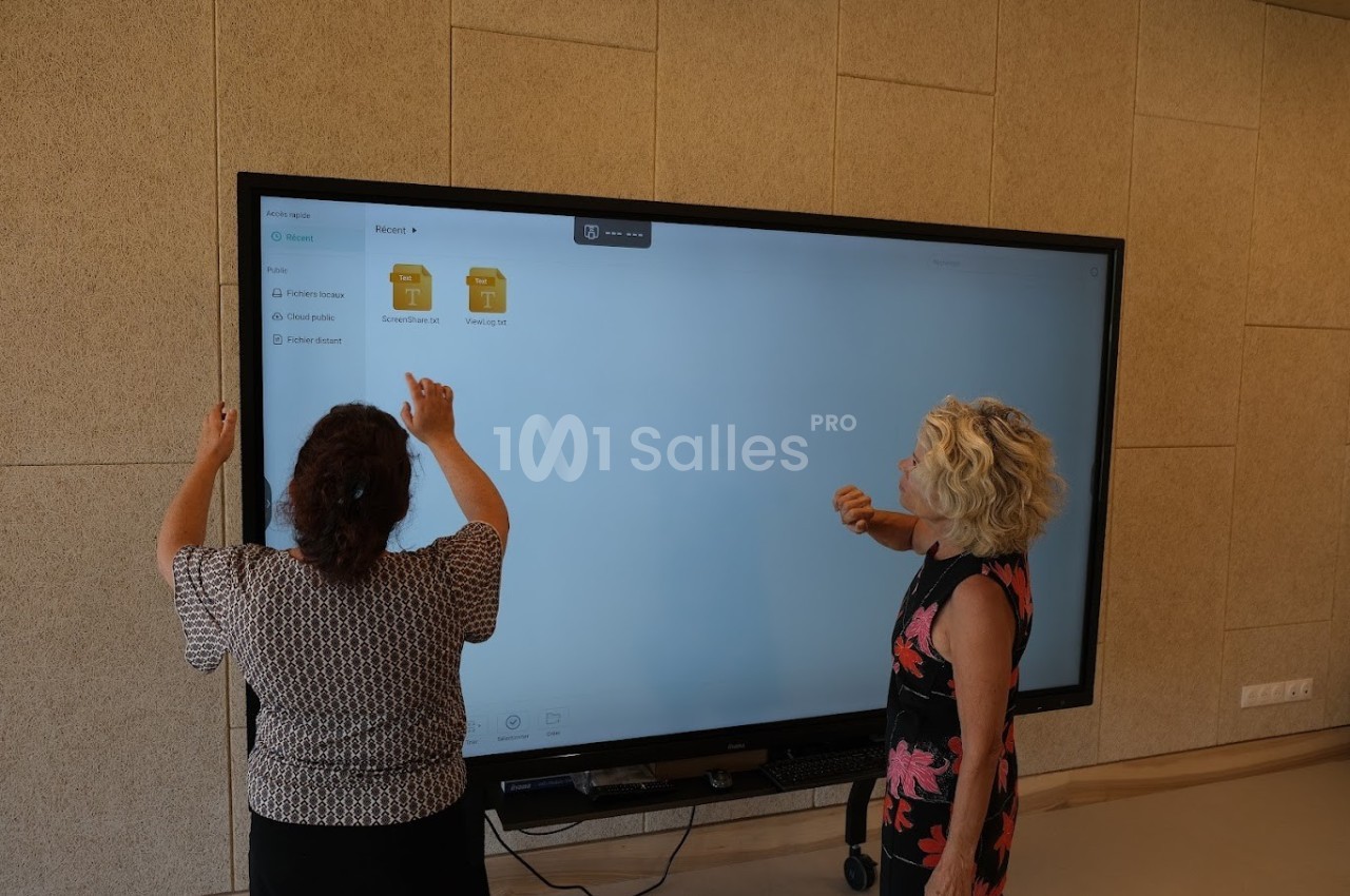 Deux femmes interagissent avec un grand écran tactile affichant des dossiers numériques dans une salle moderne.