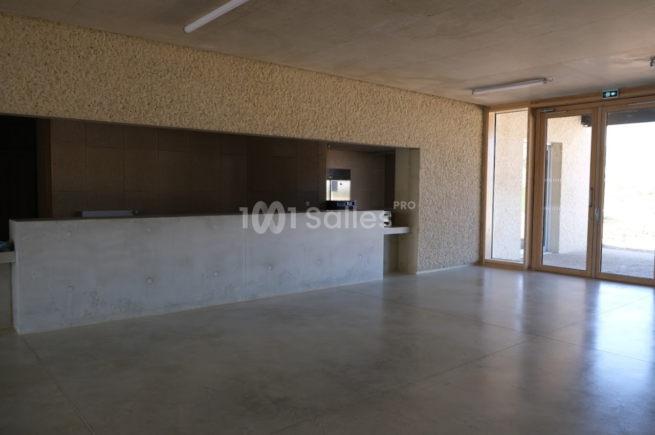 Intérieur d'un bâtiment avec un comptoir en béton, un sol en béton poli et de grandes fenêtres laissant entrer la lumière.