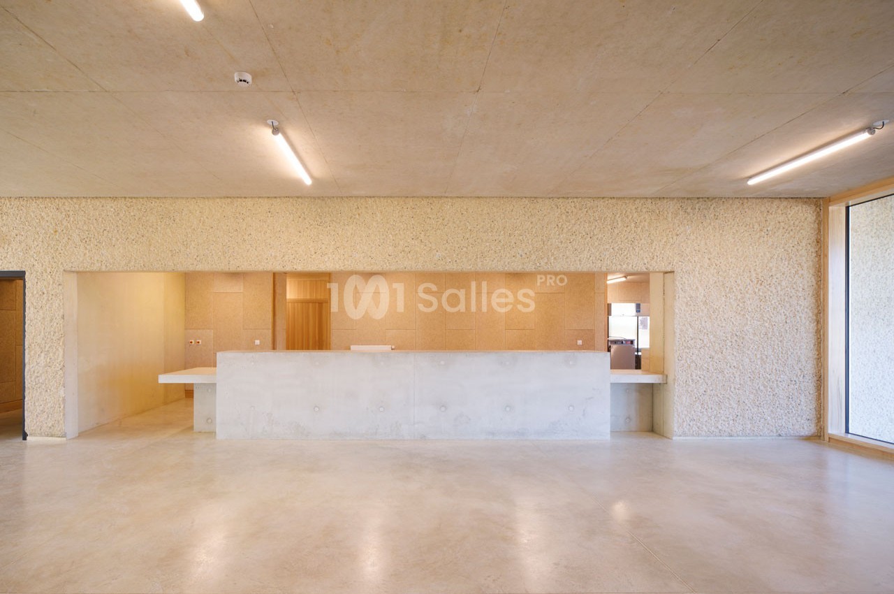 Hall avec comptoir en béton, murs texturés clairs et éclairage fluorescent, donnant sur une pièce lumineuse.