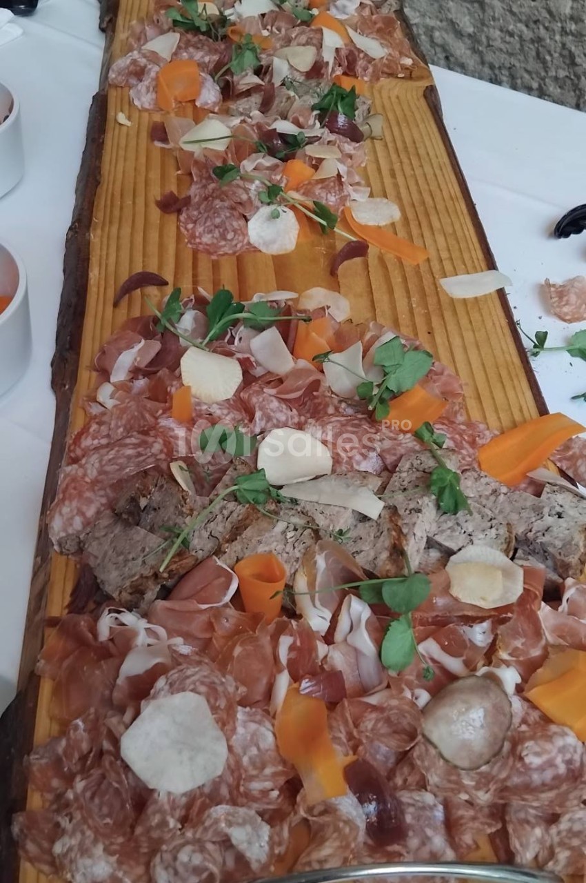 Plateau en bois garni de charcuteries variées, tranches de légumes et herbes fraîches, présenté sur une table blanche.