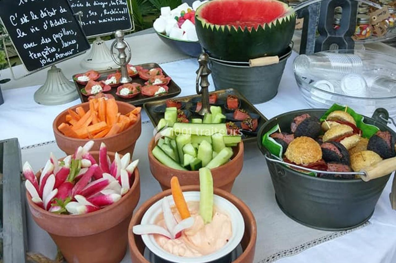 Plateau de buffet avec légumes frais, dips, tranches de pastèque, amuse-bouches et desserts disposés sur une table.