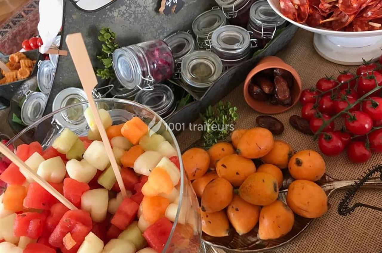 Buffet avec brochettes de fruits frais, kakis, tomates cerises, charcuterie et bocaux de condiments.