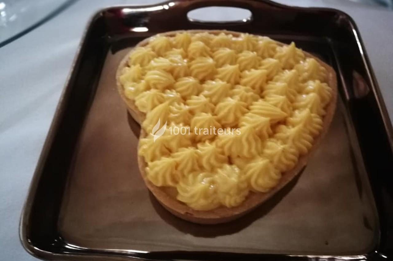 Tarte en forme de cœur garnie de crème pâtissière, présentée sur un plat rectangulaire brun.