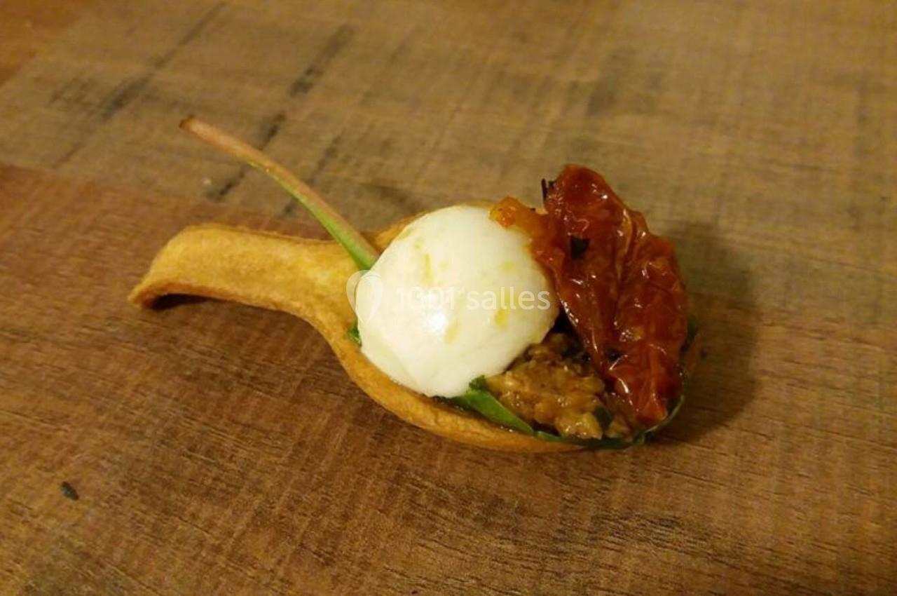 Cuillère comestible garnie de mozzarella, tomate séchée, feuille verte et préparation à base de légumes.