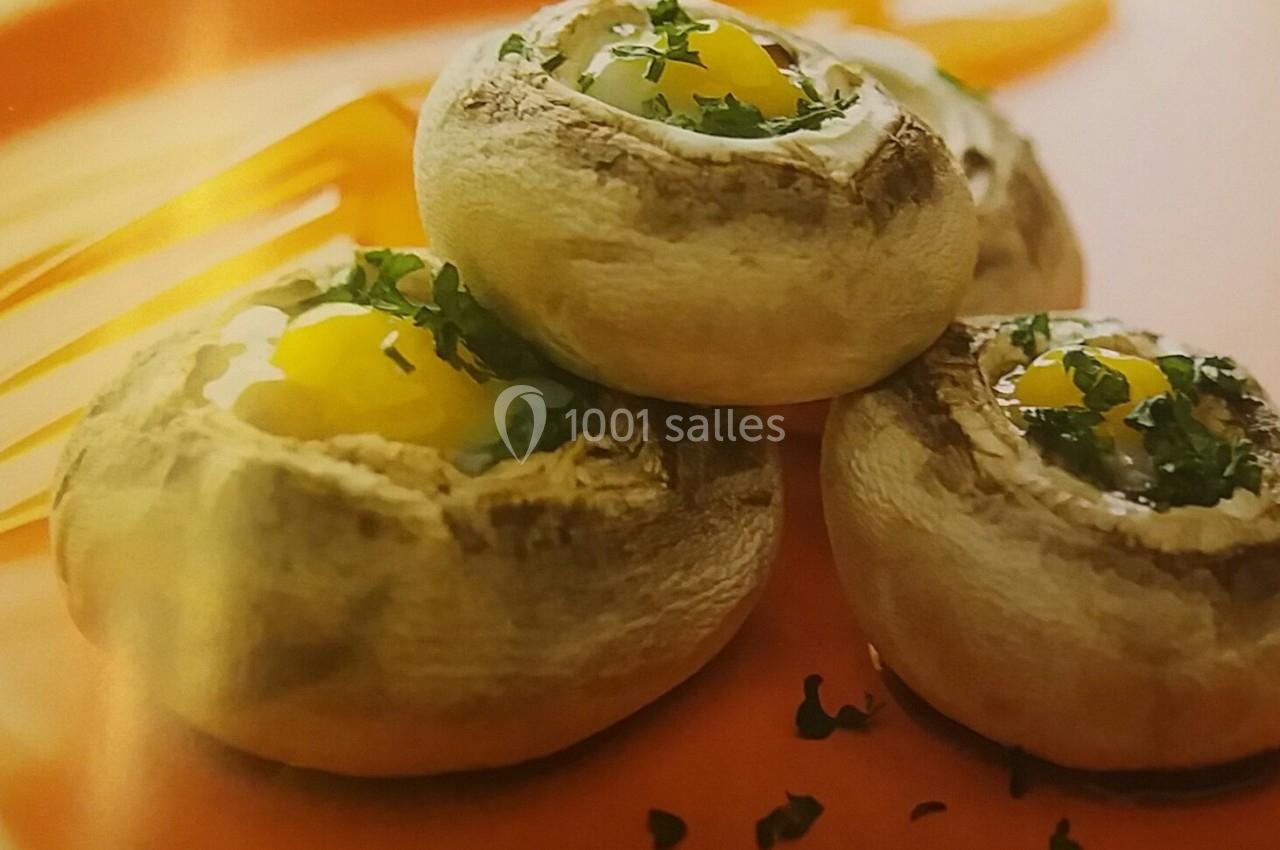 Champignons farcis avec œufs de caille et persil, présentés sur une assiette orange avec une décoration de sauce.