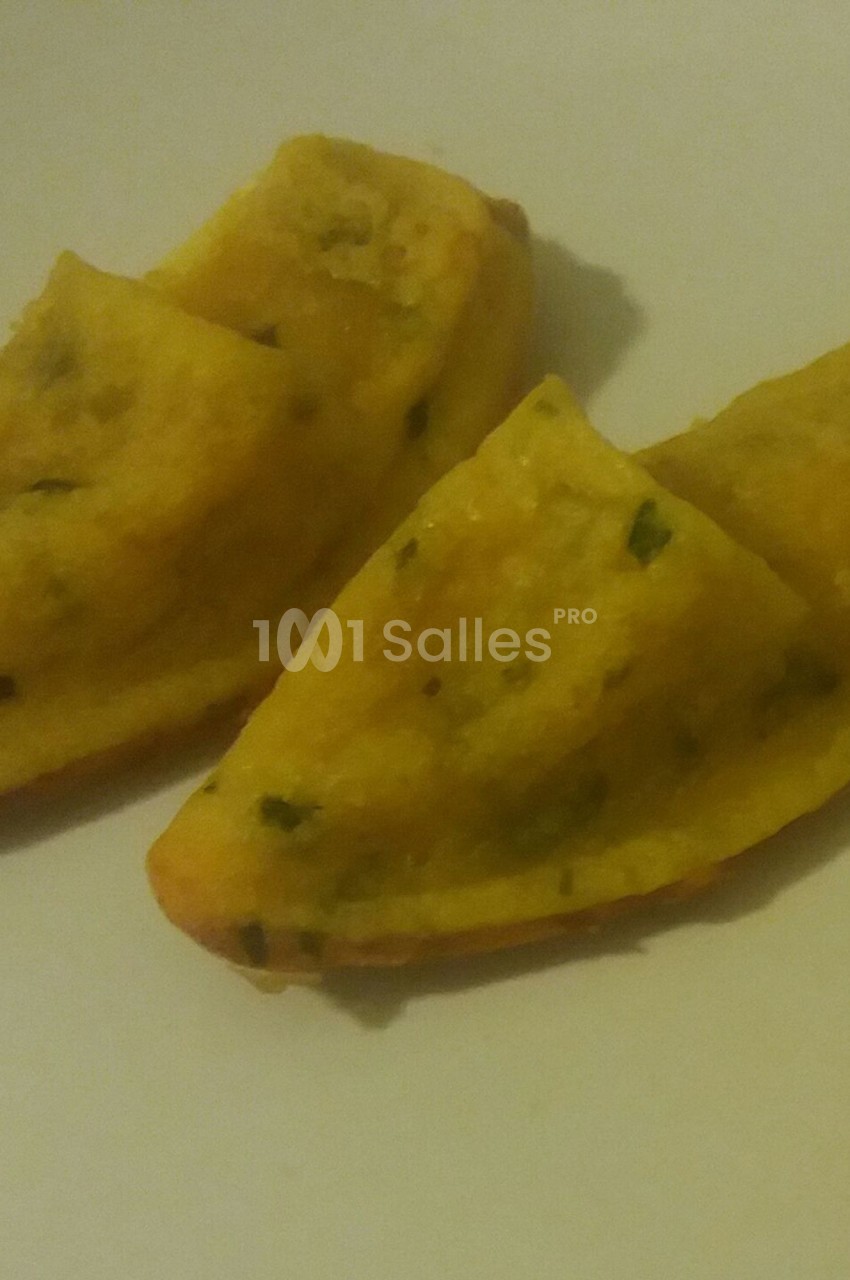 Deux beignets dorés en forme de demi-lune, garnis d'herbes, posés sur une assiette blanche.