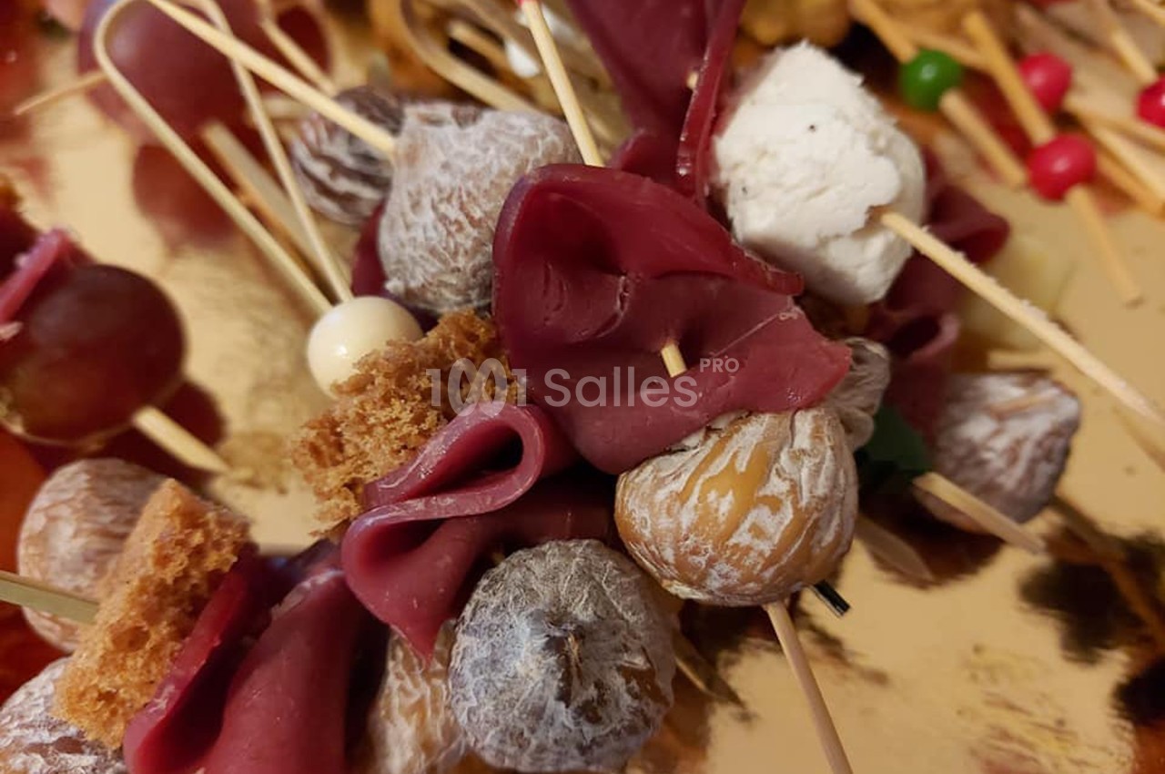 Brochettes apéritives composées de charcuterie, figues séchées, fromage frais et morceaux de pain sur un plateau doré.
