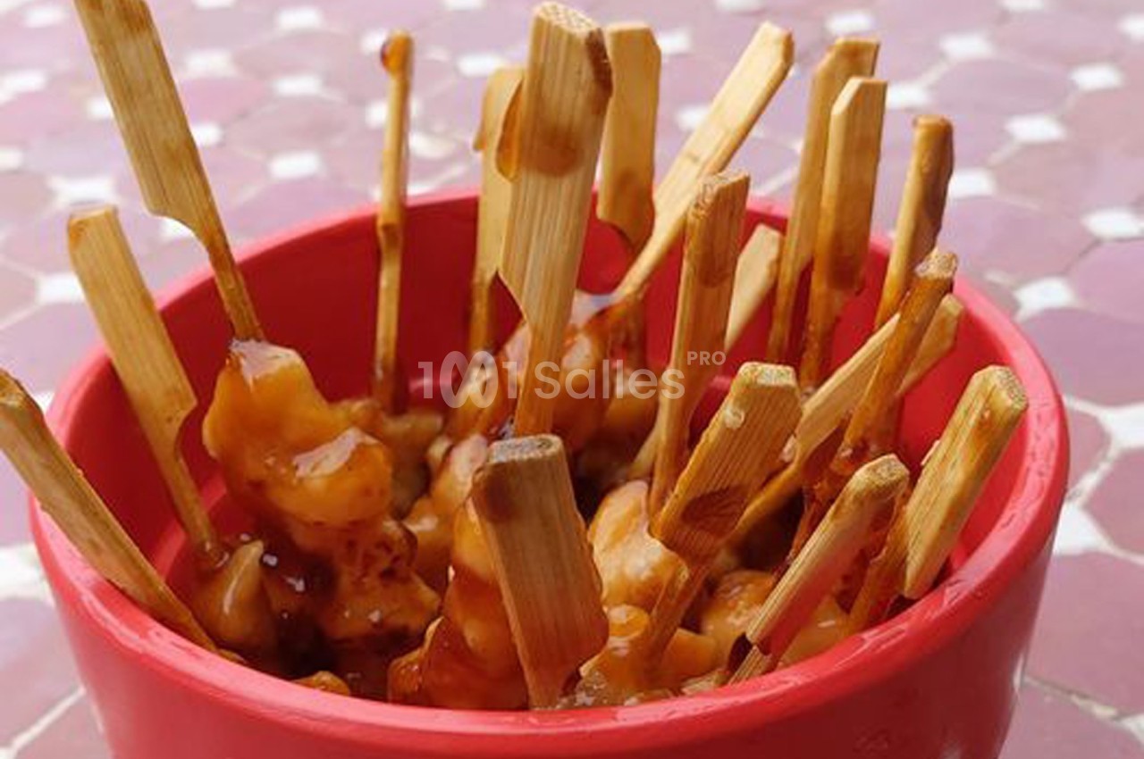 Brochettes de poulet glacées à la sauce, présentées dans un bol rouge sur une table aux motifs géométriques.