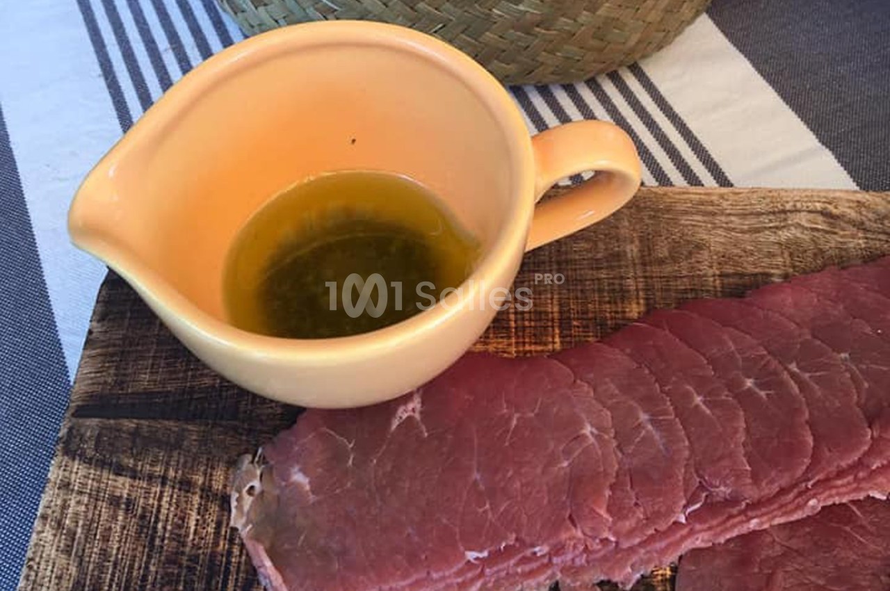 Tranches de viande crue sur une planche en bois avec une saucière contenant une sauce verte.