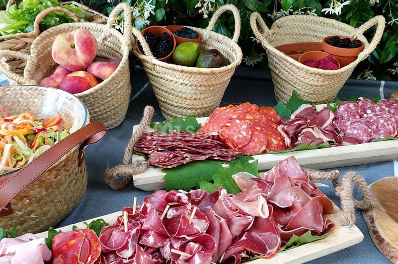 Plateaux de charcuterie variée et paniers de fruits frais disposés sur une table en extérieur.