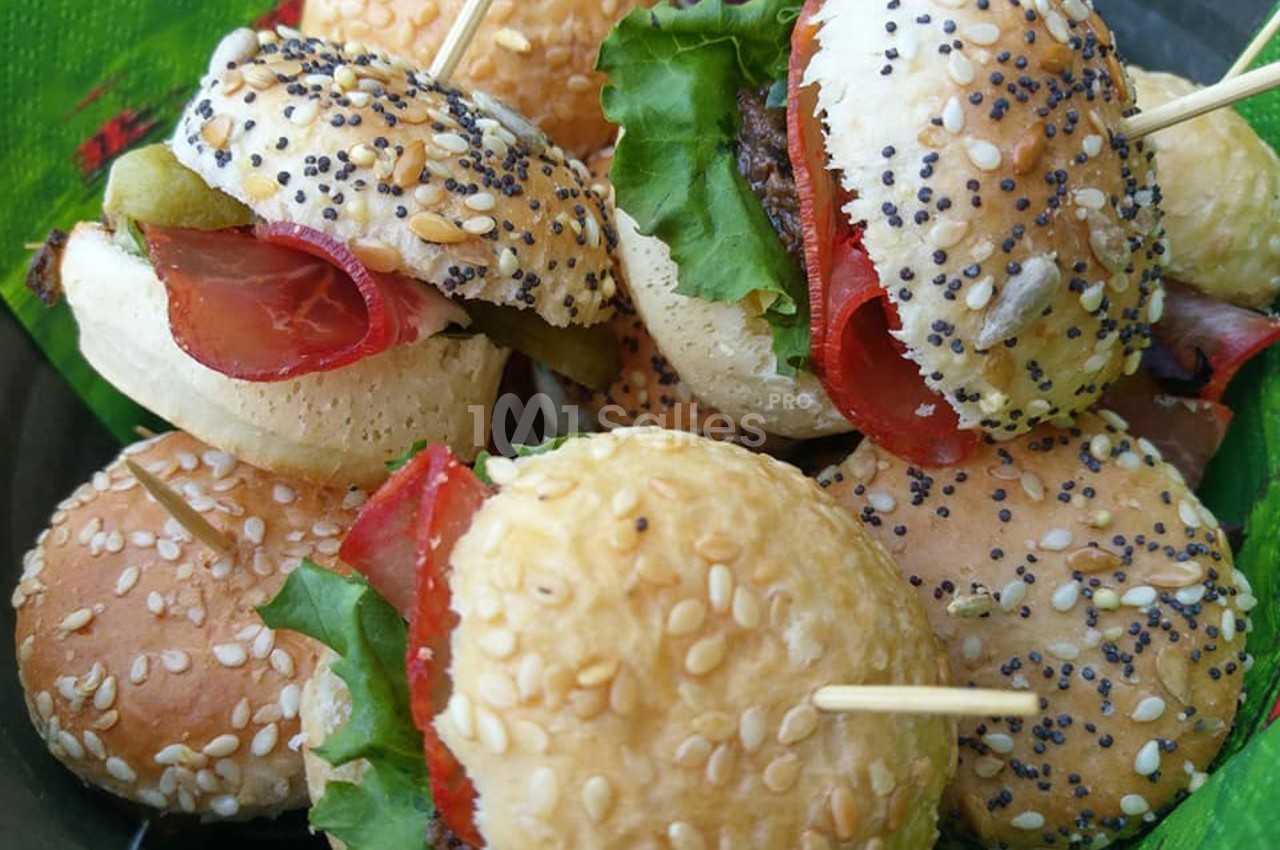 Mini-burgers garnis de salade, charcuterie et légumes, présentés sur un plateau avec des piques en bois.
