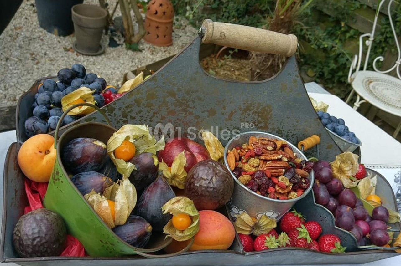 Plateau en métal contenant un assortiment de fruits frais, noix et baies, posé sur une table en extérieur.