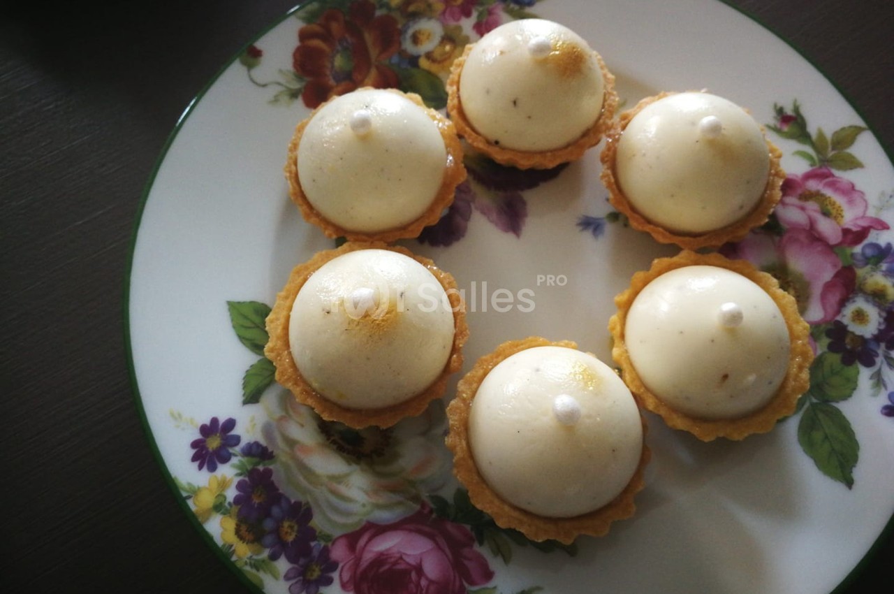 Assortiment de tartelettes garnies de mousse blanche, présentées sur une assiette décorée de motifs floraux.