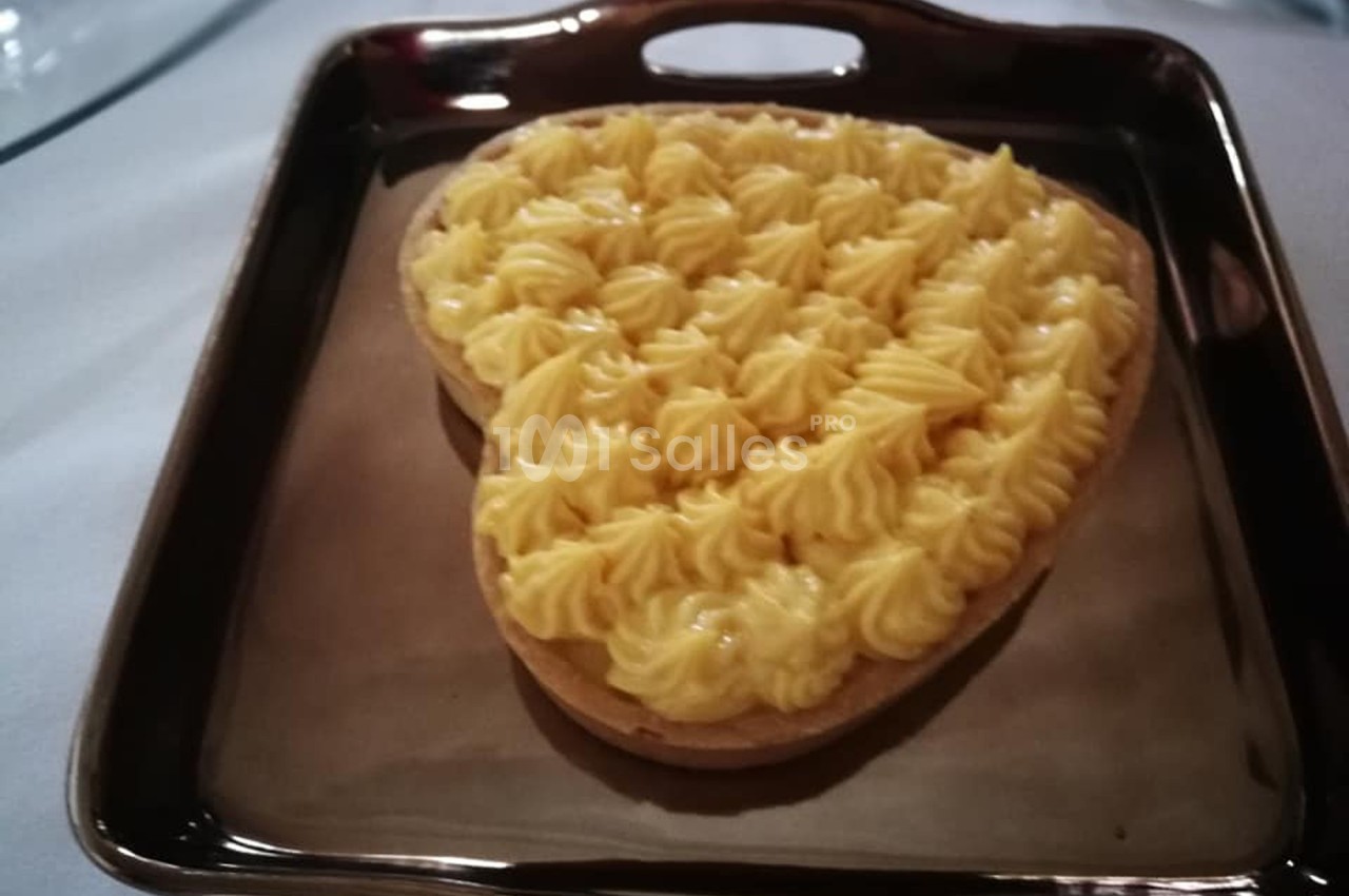 Tarte en forme de cœur garnie de crème pâtissière, présentée sur un plat rectangulaire brun.