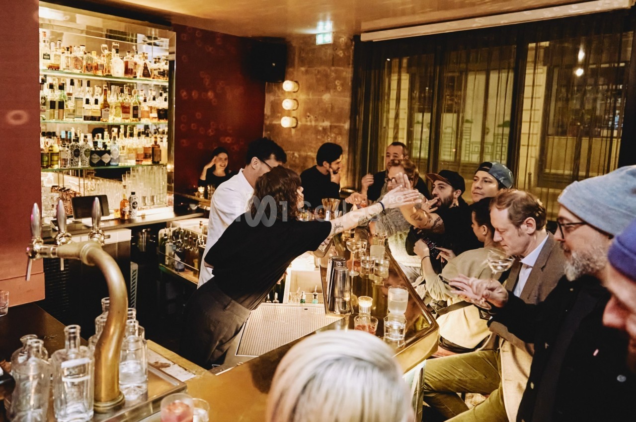 Un bar animé avec des clients discutant et un barman servant des boissons derrière le comptoir.