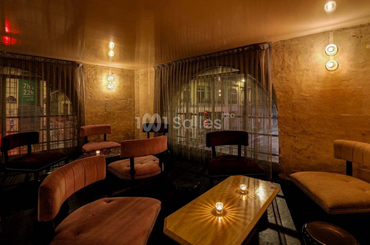 Espace intérieur chaleureux avec fauteuils, table basse en bois et bougies, éclairé par des lumières tamisées.