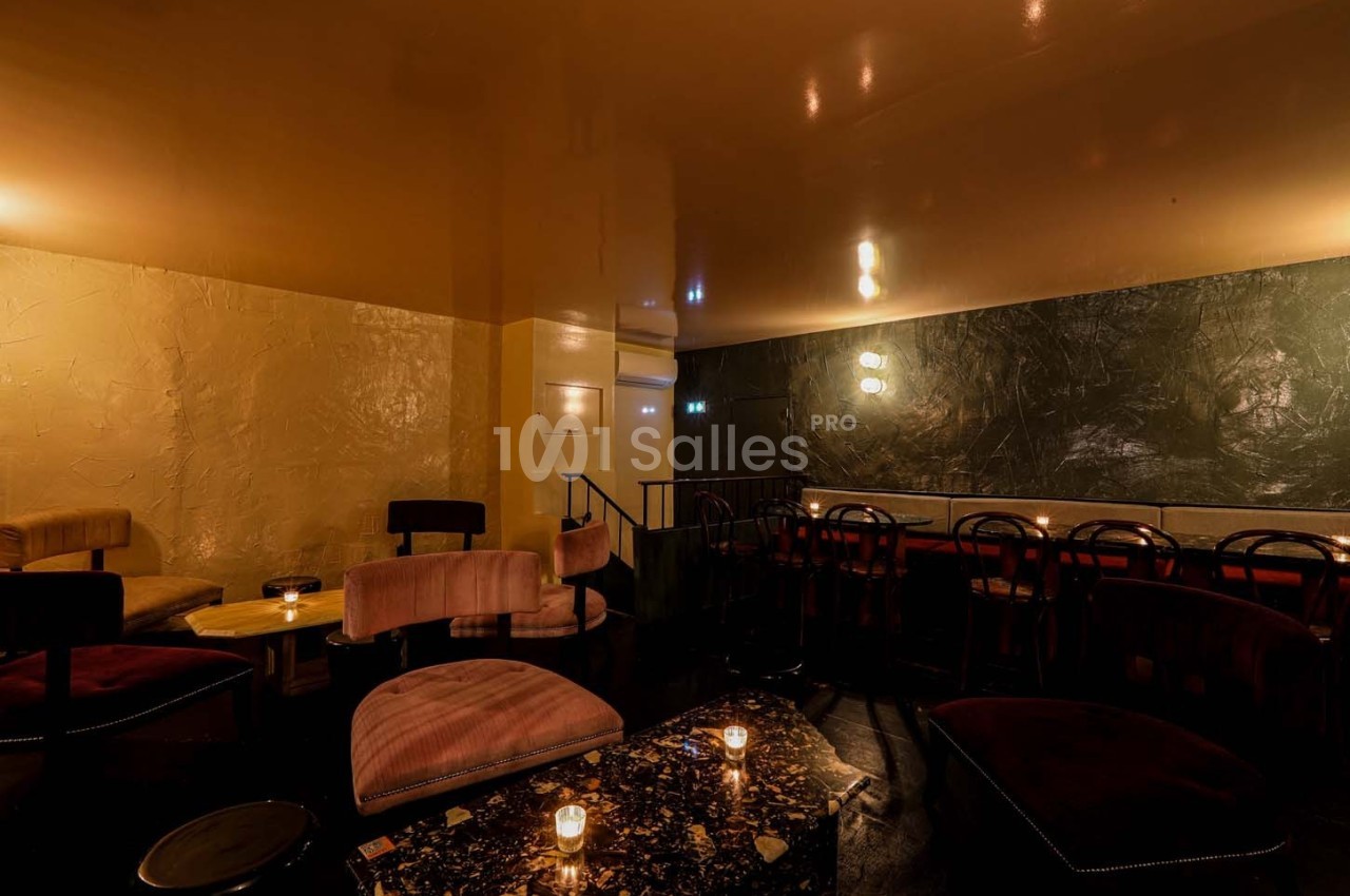 Salle de bar tamisée avec des fauteuils en velours, des tables basses et des murs aux textures contrastées.