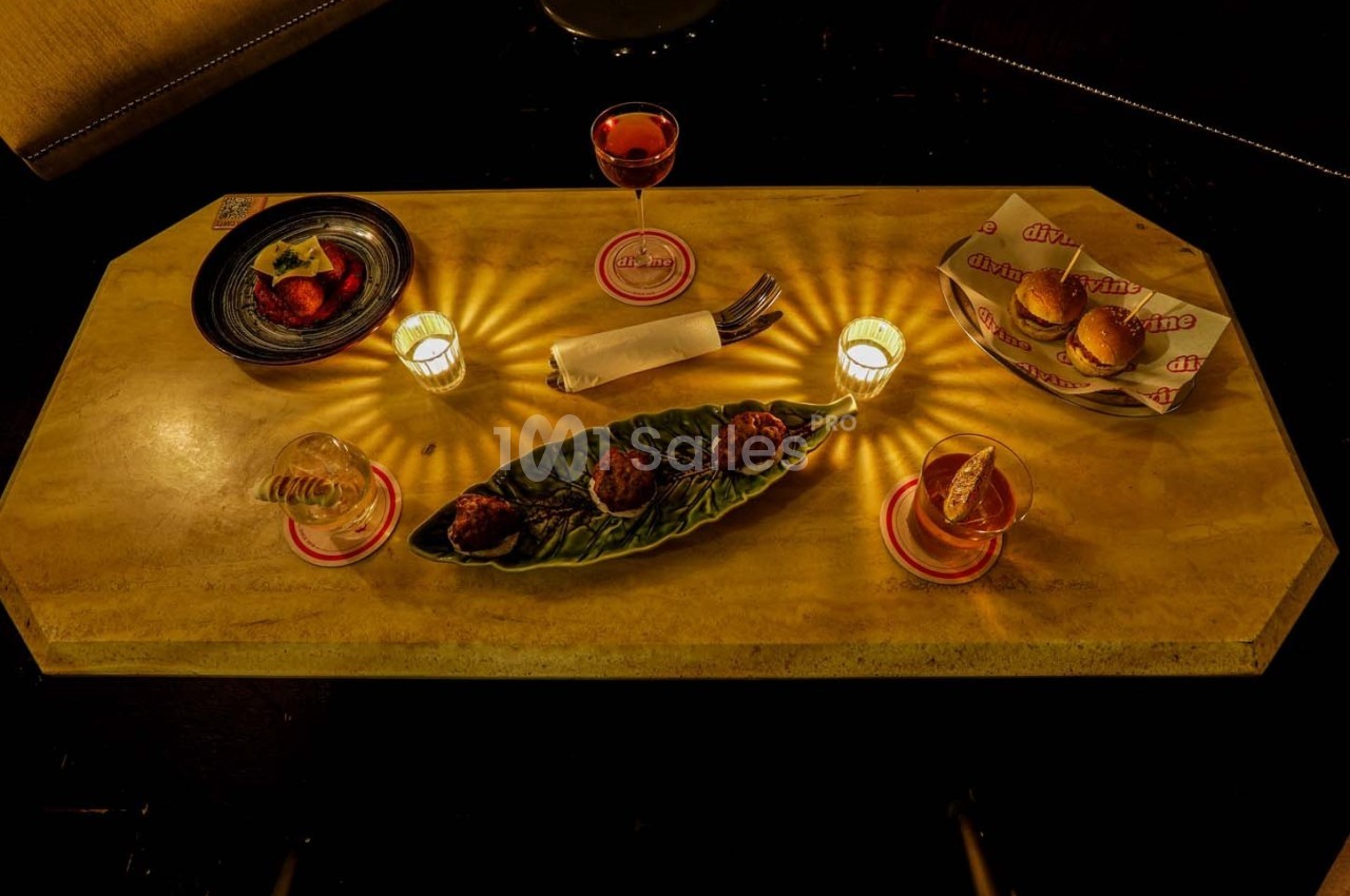 Table dressée avec des amuse-bouches, verres de boisson, bougies allumées et serviette pliée sur une nappe beige.