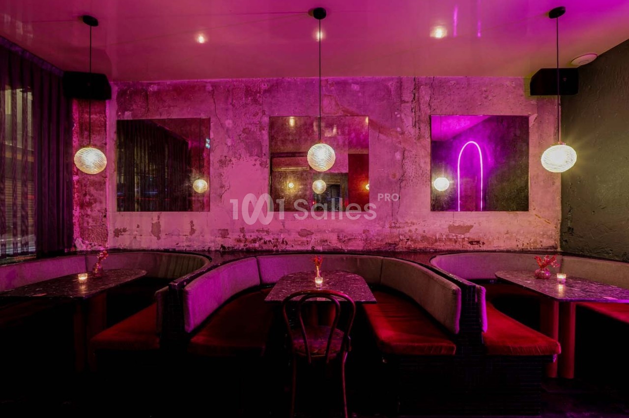 Salle de restaurant avec banquettes rouges, tables en marbre noir, éclairage tamisé et murs au style brut.