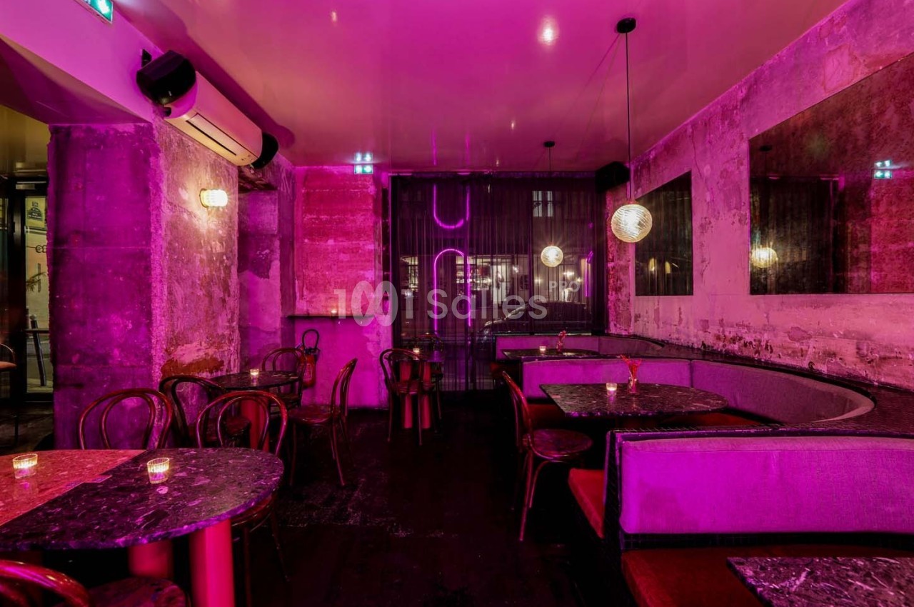 Salle de restaurant avec éclairage rose, tables en marbre, chaises en bois et banquettes contre un mur texturé.