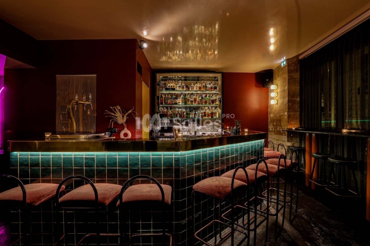 Bar élégant avec comptoir carrelé, tabourets rembourrés, étagères remplies de bouteilles et éclairage tamisé.