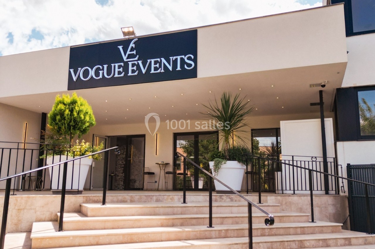 Façade d'un bâtiment moderne avec enseigne ’Vogue Events’, escalier et plantes en pots devant l'entrée.