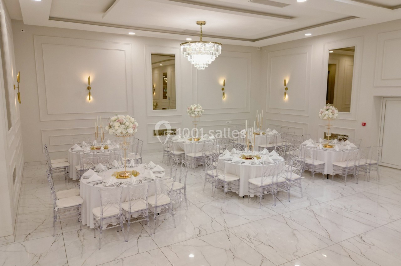 Salle de réception lumineuse avec tables rondes décorées de nappes blanches, chaises transparentes et centres de table…