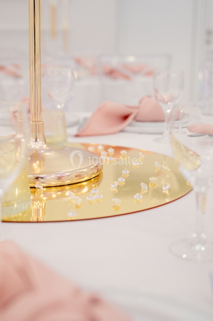 Centre de table doré décoré de perles et cristaux, entouré de serviettes roses et verres élégants.