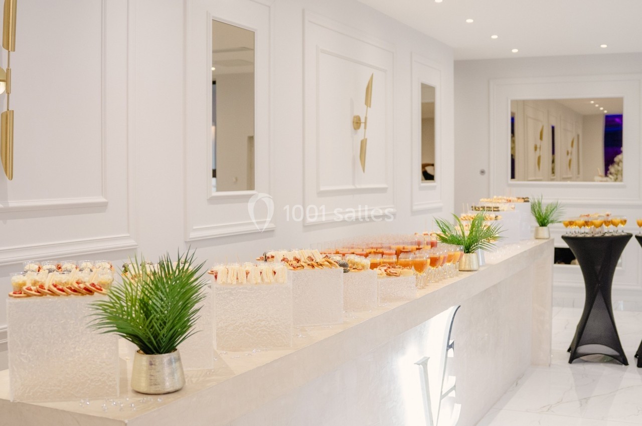 Buffet élégant avec desserts variés disposés sur une table blanche, décorée de plantes et éclairée par des appliques murales.
