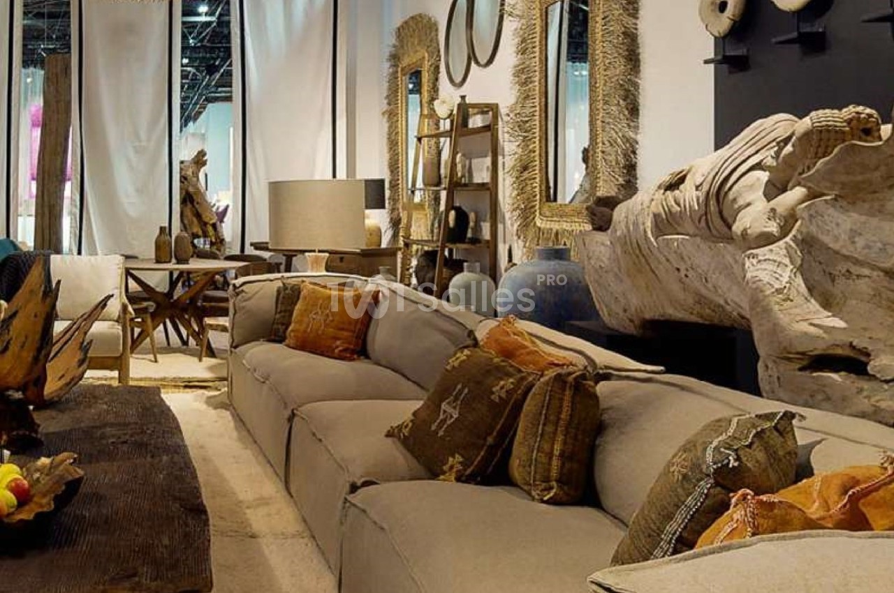 Canapé beige avec coussins décoratifs dans un salon aménagé avec des objets en bois et des miroirs encadrés.