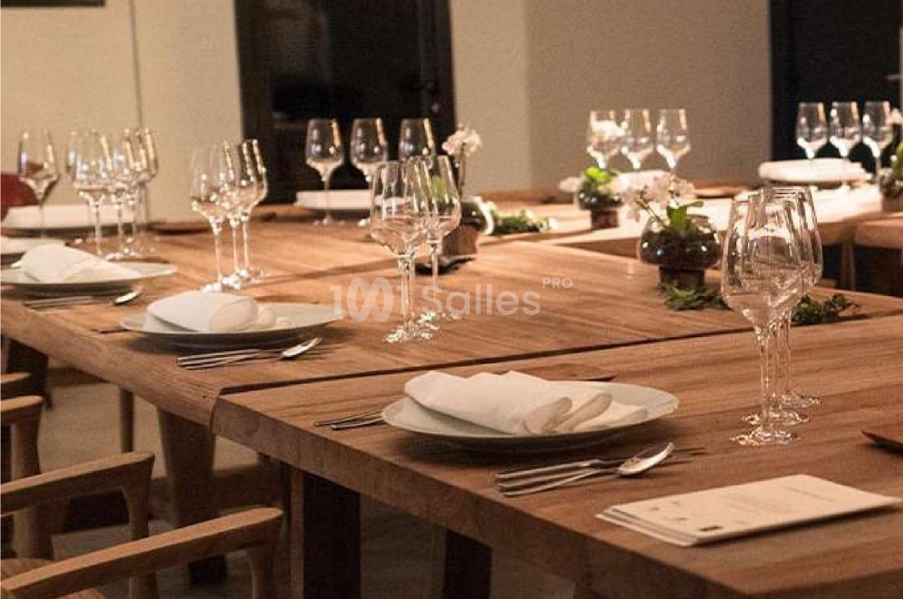 Table en bois dressée avec des assiettes, serviettes pliées, couverts et verres, dans une salle élégamment éclairée.
