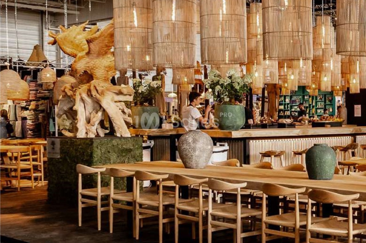 Salle de restaurant avec tables en bois, chaises assorties, sculptures et suspensions lumineuses en osier.