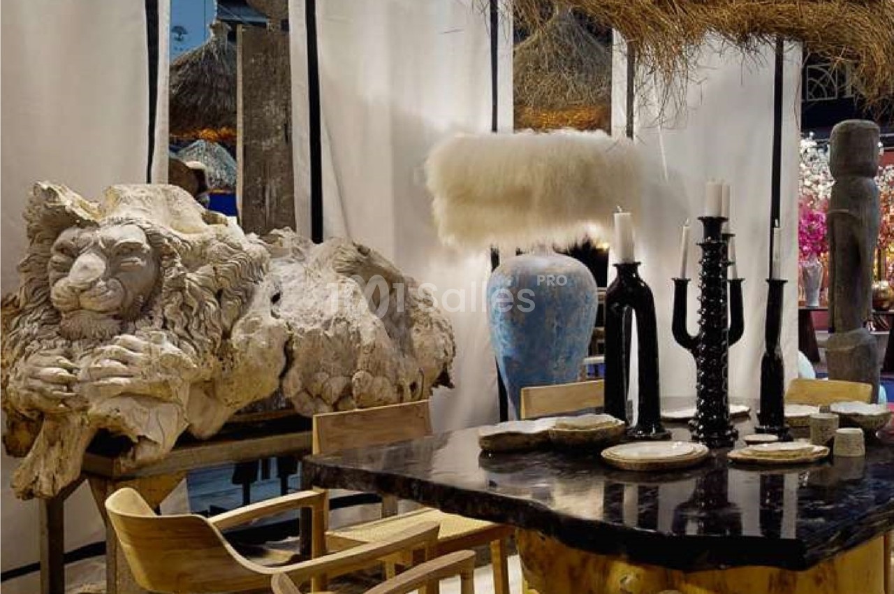 Sculpture de lion en pierre, table en bois sombre avec chandeliers noirs, vase bleu et décor rustique en arrière-plan.