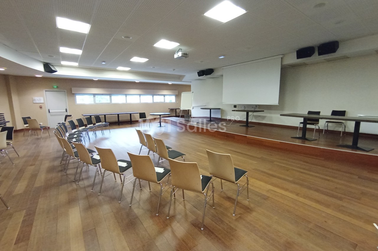 Salle de conférence vide avec des chaises disposées en arc de cercle, un projecteur et un écran blanc.