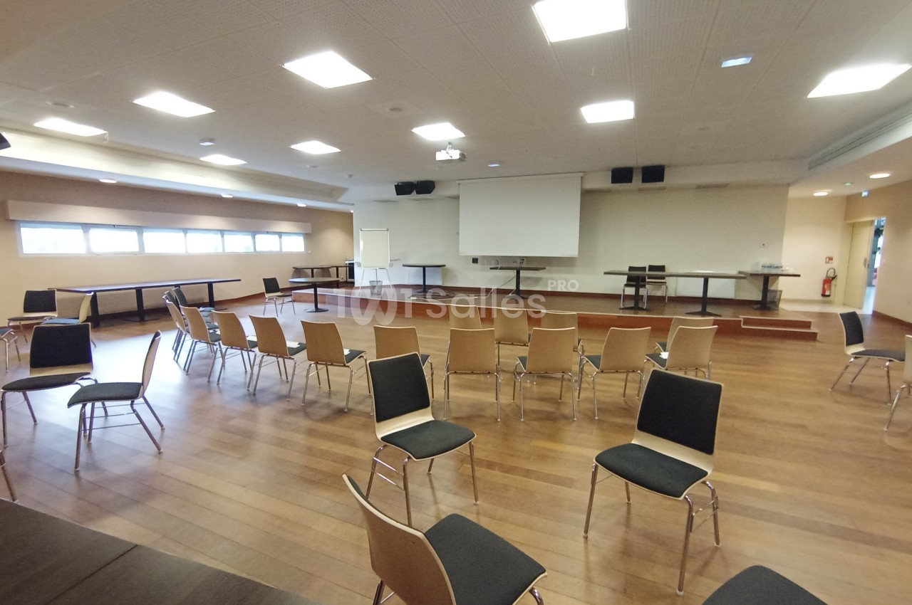 Salle de conférence lumineuse avec des chaises disposées en cercle, un écran de projection et une estrade en bois.