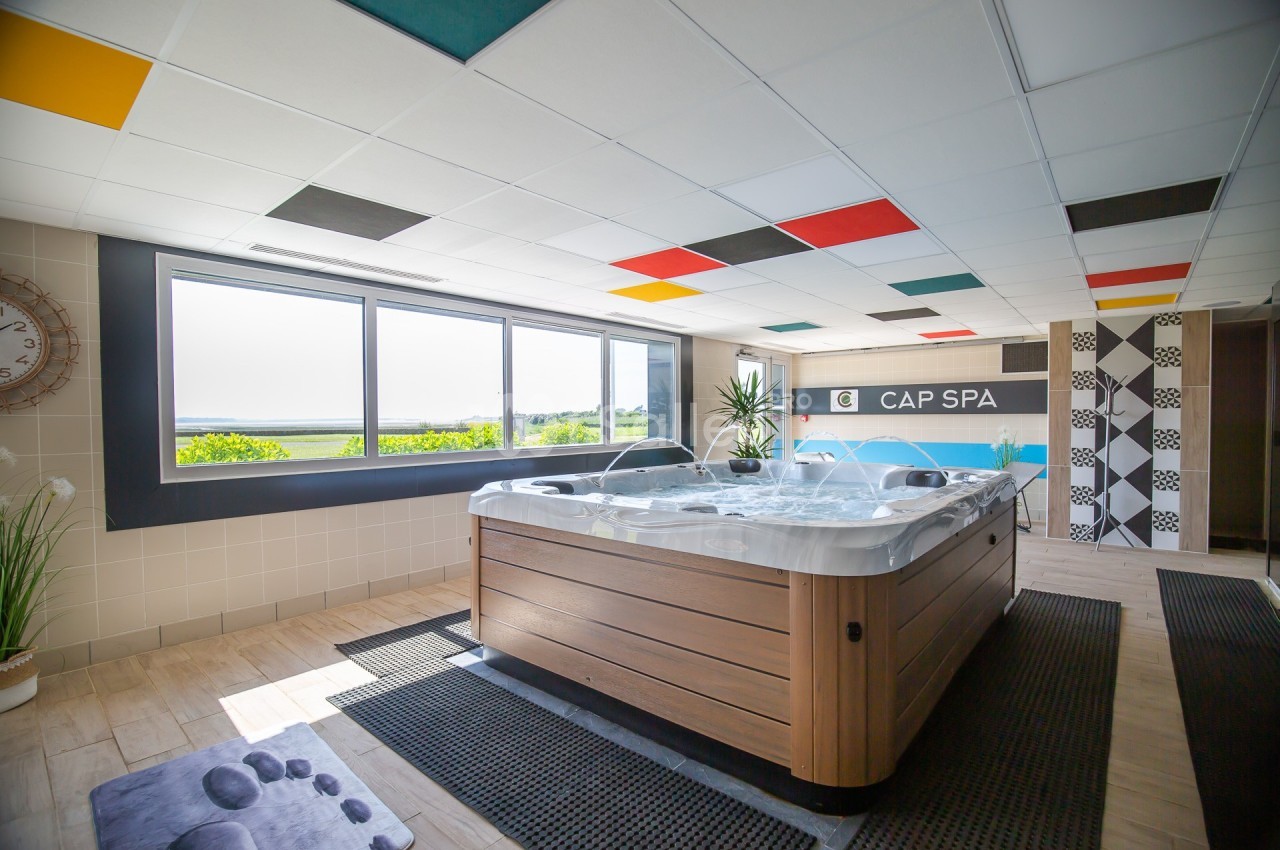 Jacuzzi moderne dans une pièce lumineuse avec vue sur la nature, décorée de carreaux et de panneaux colorés.
