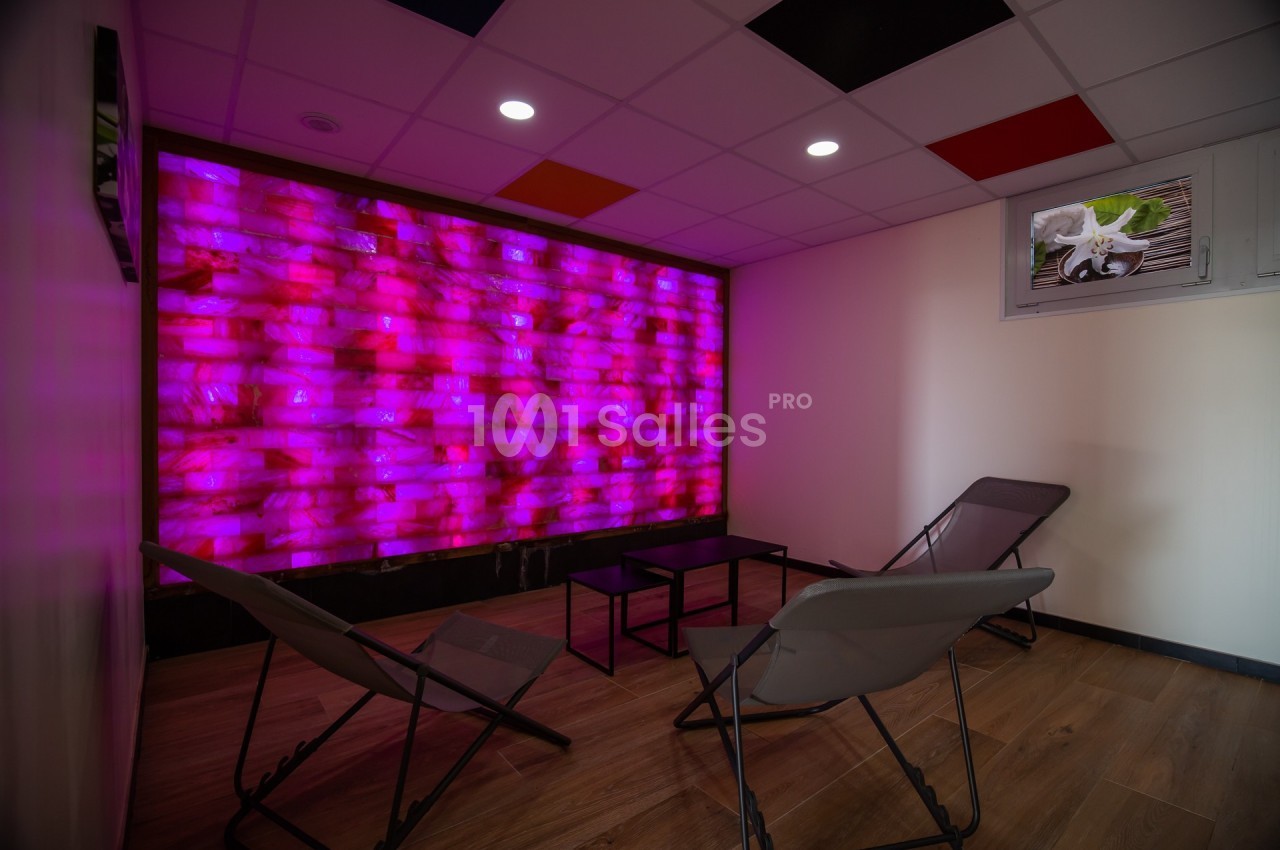 Salle de détente avec mur lumineux rose, chaises longues grises et sol en bois clair.