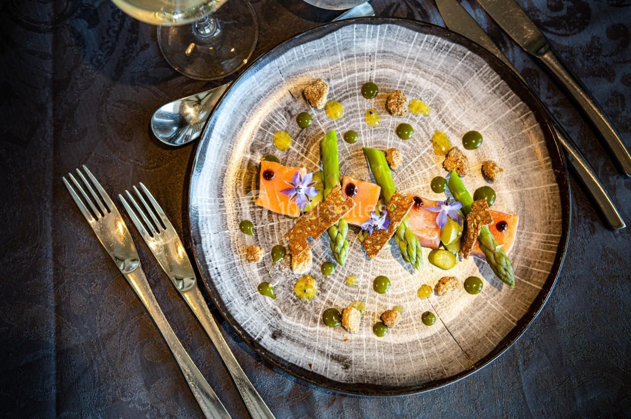 Assiette gastronomique avec saumon, asperges, fleurs comestibles et sauces disposées artistiquement.