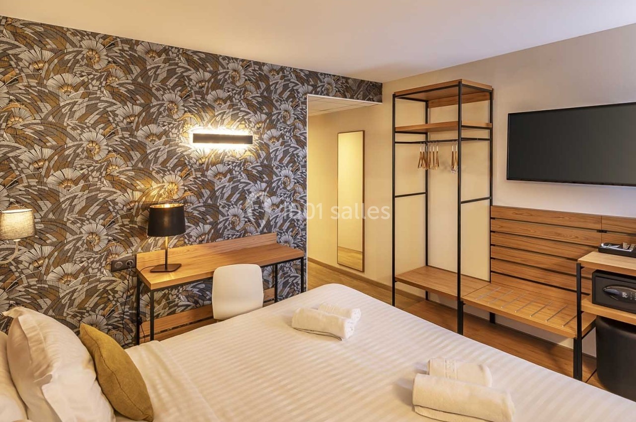 Chambre d'hôtel moderne avec lit double, bureau, téléviseur mural, portant, et décoration murale à motifs floraux.